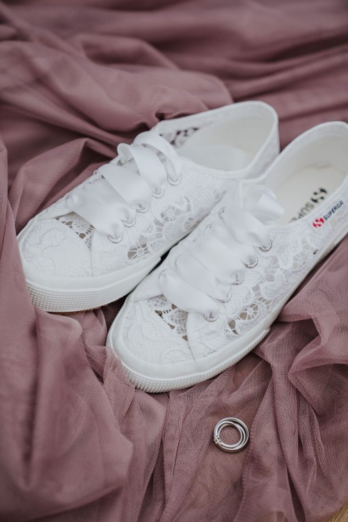 Weiße Brautschuhe und die Ringe liegen auf einem rosa Stoff.