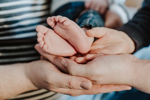 Baby Füße werden von der gesamten Familie mit deren Händen drunter festgehalten.