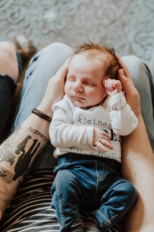 Ein kleines Baby liegt auf dem Schoß des Vaters und wird mit seinem Händen festgehalten.