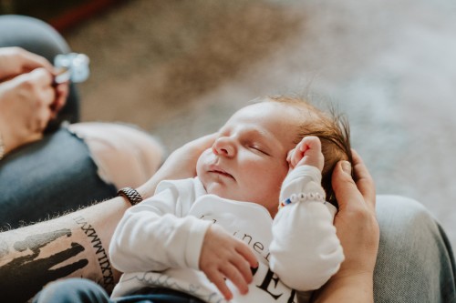 Ein kleines Baby liegt auf dem Schoß des Vaters und wird mit seinem Händen festgehalten.