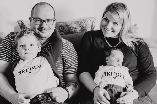 Eine Frau und ein Mann sitzen mit zwei kleinen Kindern auf der Couch.