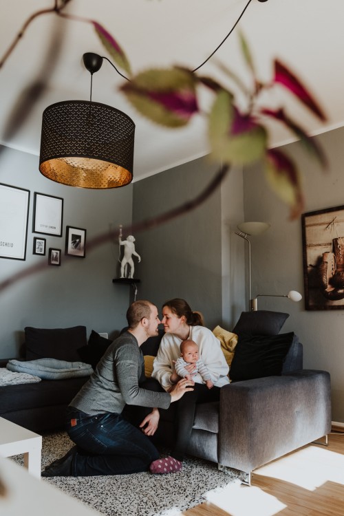 Eine Frau sitzt auf der Couch und hält ein Baby auf ihrem Schoß, während der Mann vor der Couch kniet.