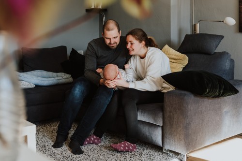 Eine Frau und ein Mann sitzen auf der Couch und halten ein Baby in der Mitte.