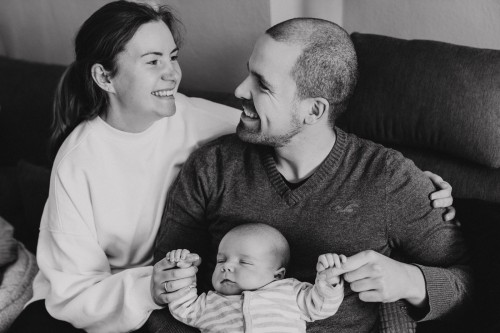 Eine Frau und ein Mann sitzen mit einem Baby auf der Couch.