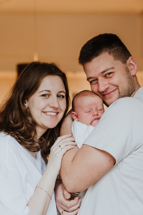 Eine Frau und ein Mann halten ein Baby in der Mitte und posieren für ein Familienfoto.