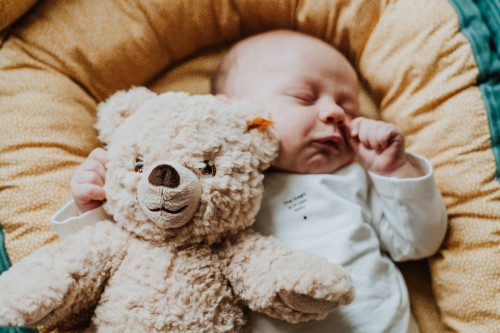 Ein Baby schläft im Bettchen zusammen mit einem Plüschbär.