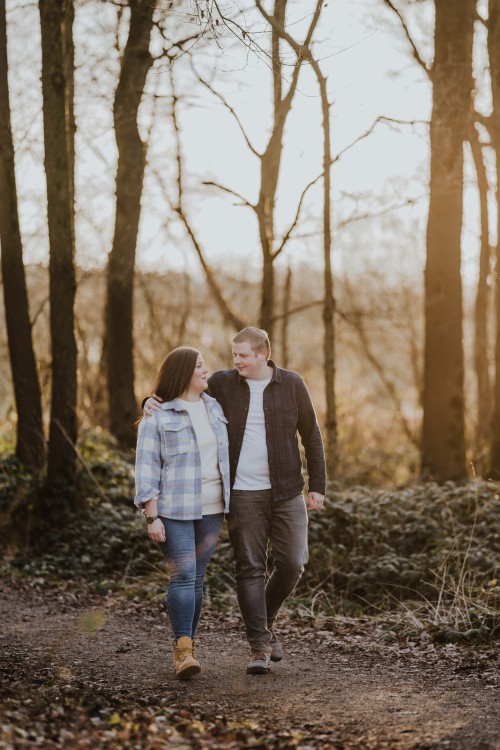 Eine Frau und ein Mann gehen umarmt einen Waldweg entlang.