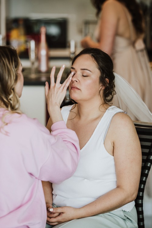 Eine Braut wird von einer Frau geschminkt.