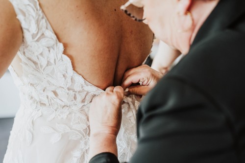 Eine Frau hilft der Braut beim Anziehen des Kleides.