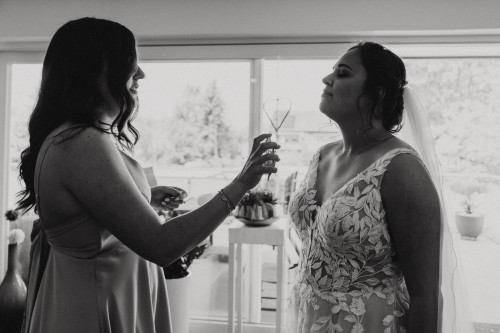 Eine Frau richtet ein Parfum Flakon auf eine Braut.
