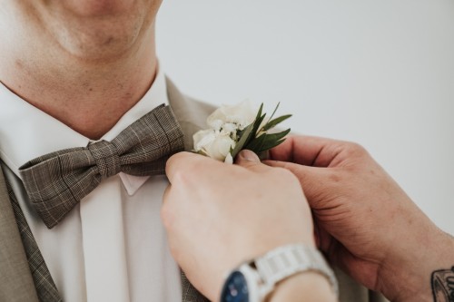 Zwei Hände stecken einen Blumenanstecker am Anzug des Bräutigams an.
