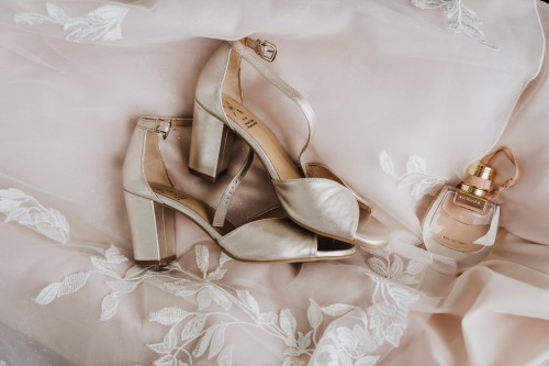 Schuhe und ein Parfüm Flakon liegen auf einem Brautkleid.