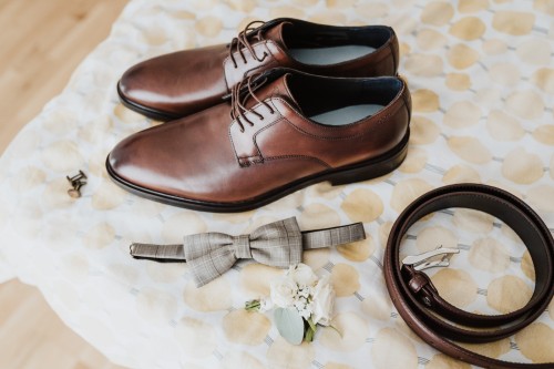 Schuhe, Gürtel, Fliege, Blumenanstecker und Manschettenknöpfe auf einer Decke.