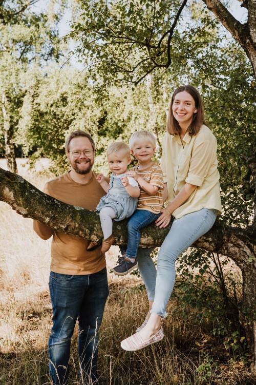 Eine Frau und zwei kleine Kinder sitzen auf einem Ast, während ein Mann dahinter steht.