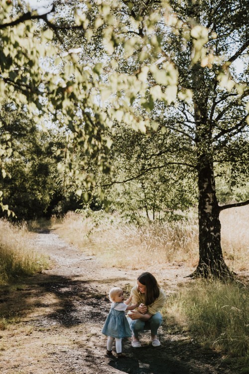 Eine Frau hockt auf einem Feldweg neben einem kleinen Mädchen.