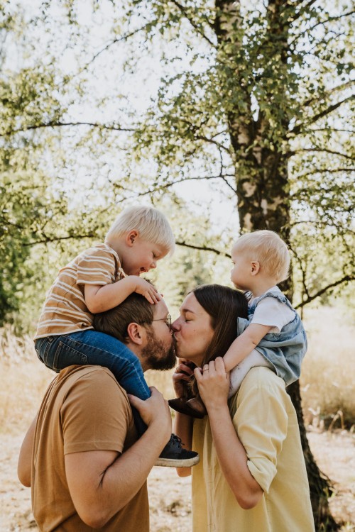 Ein Mann und eine Frau halten die Kinder huckepack und geben sich dabei ein Küsschen.
