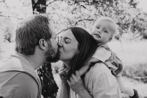 Ein Mann und eine Frau küssen sich, während die Frau ein Baby auf ihrem Rücken hält.