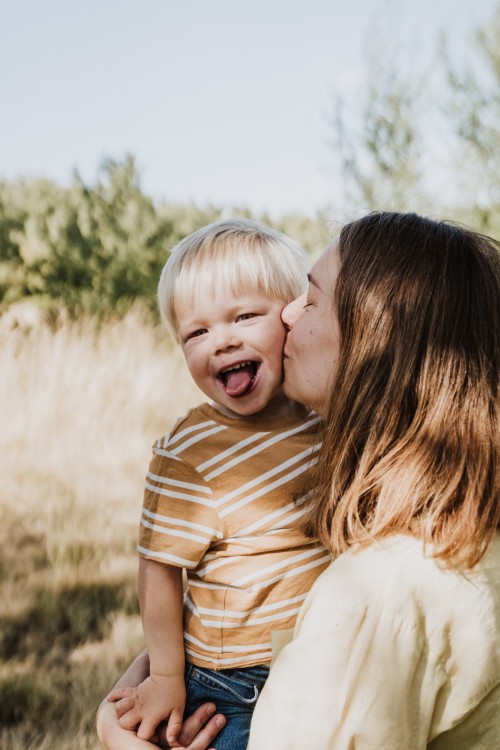 Eine Frau gibt einem Jungen einen Kuss auf die Wange und er zeigt seine Zunge.
