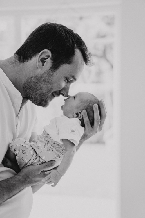 Ein Mann hält ein Baby hoch und berührt mit seiner Nase die Nase des Kindes.
