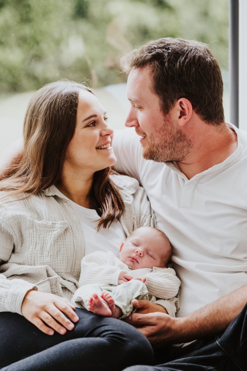 Eine Frau und ein Mann sitzen auf der Couch und halten ein Baby.