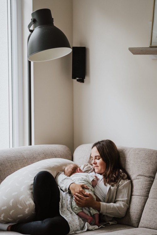 Eine Frau liegt auf der Couch und hält ein Baby auf ihrem Bauch.