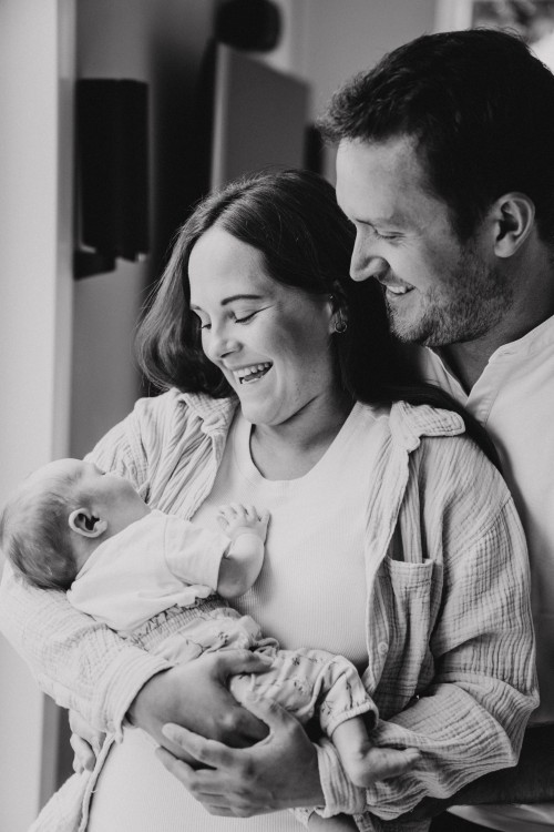 Eine Frau die ein Baby auf dem Arm hält, wird von einem Mann angekuschelt.