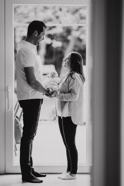 Ein Mann und eine Frau stehen vor einer Glastür und halten zusammen ein Baby.