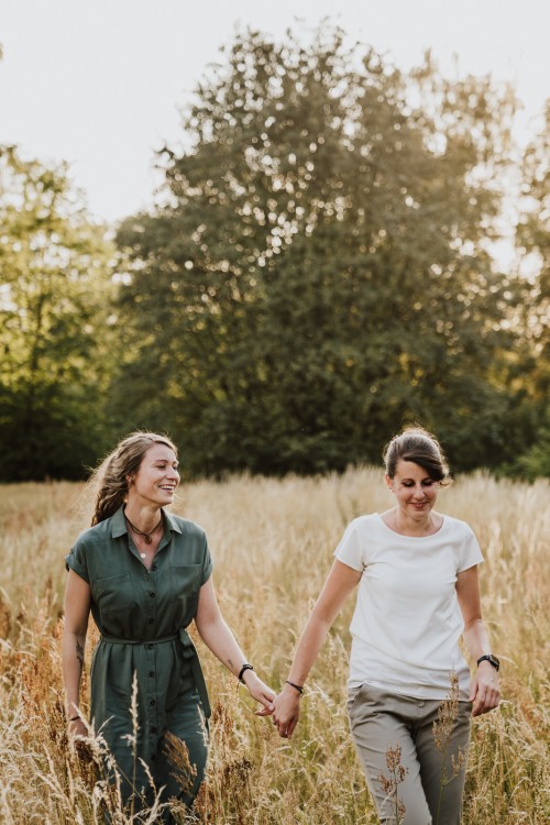 Zwei Frauen laufen durch ein Feld und halten Händchen.