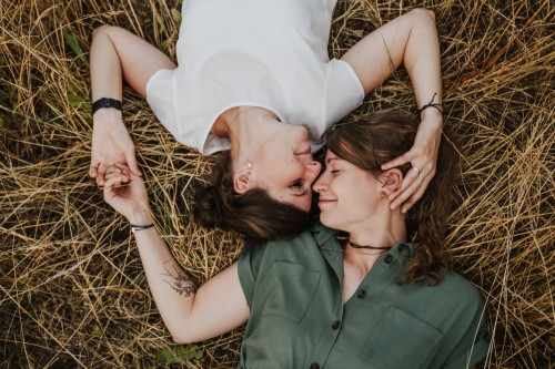 Zwei Frauen liegen im hohen Gras und kuscheln.