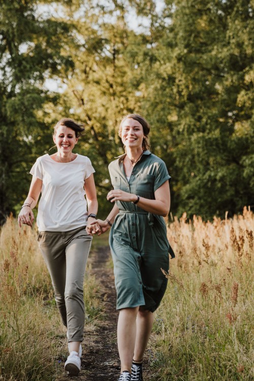 Zwei Frauen laufen einen Feldweg entlang und halten Händchen.