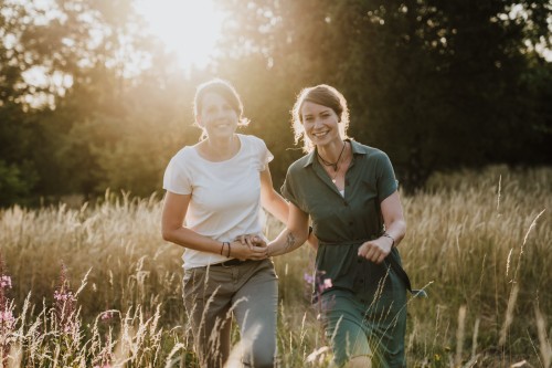 Zwei Frauen laufen durch eine Wiese und halten Händchen.