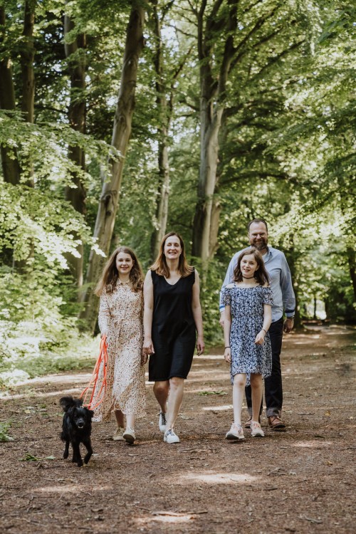 Ein Mann, eine Frau und zwei Mädels spazieren mit einem Hund durch einen Wald.