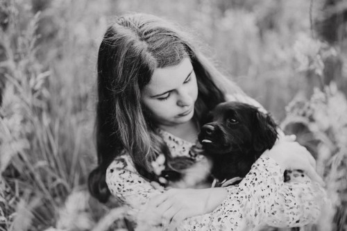 Ein Mädchen sitzt auf einer Wiese und hält einen kleinen Hund.