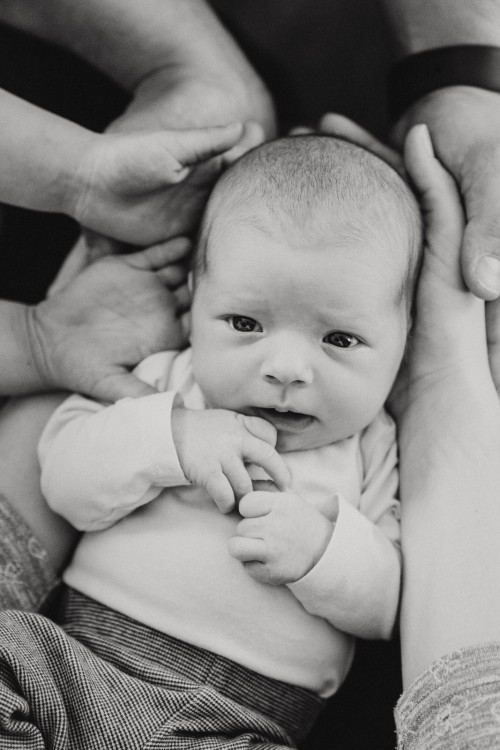Ein Baby liegt auf den Händen der Eltern und der kleinen Schwester.