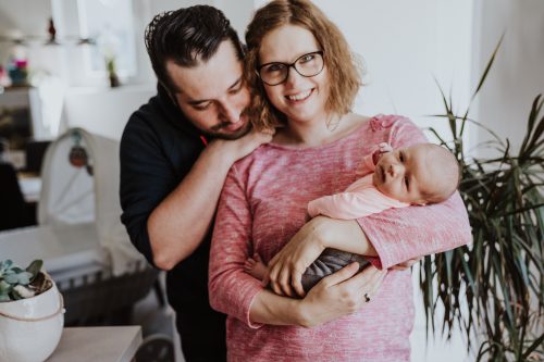Eine Frau hält ein kleines Baby auf dem Arm und wird von einem Mann umarmt.
