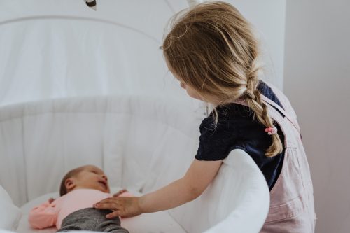 Ein kleines Mädchen streichelt ein kleines Baby, das in einer Wiege liegt.