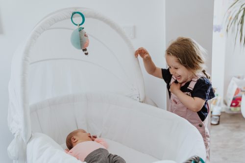 Ein kleines Mädchen steht vor einem Babybett.