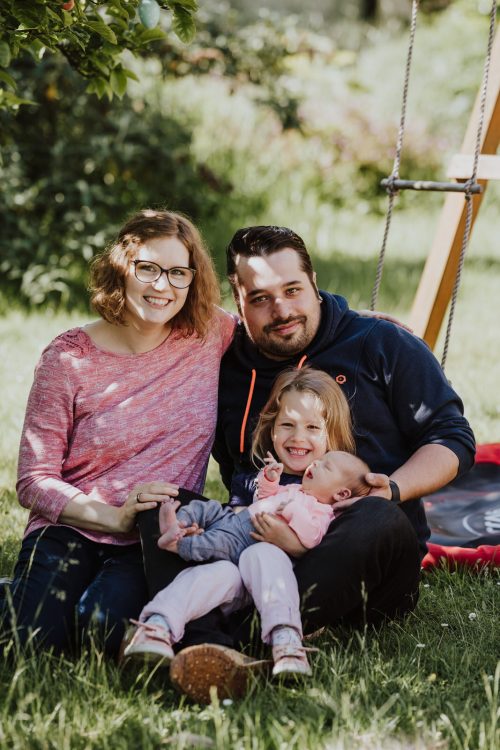 Ein Pärchen sitzt auf der Wiese mit einem Baby und einem kleinen Mädchen.