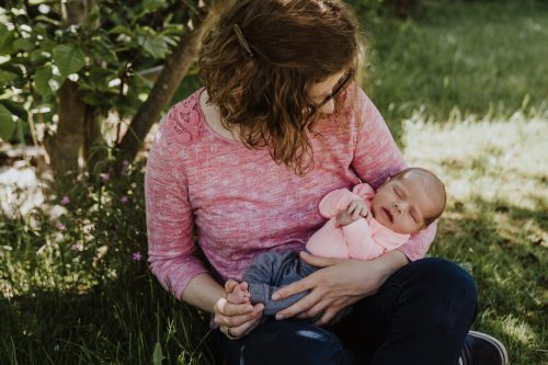Eine Frau sitzt unter einem Baum und hält ein kleines Baby auf dem Arm.
