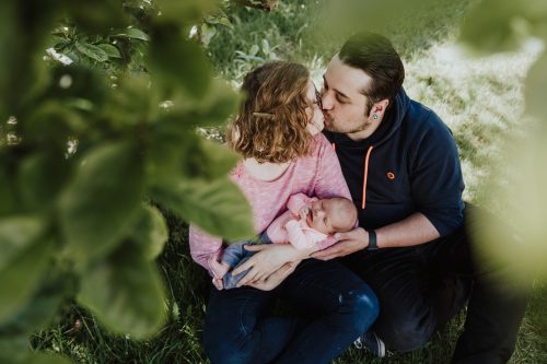 Ein Pärchen sitzt unter einem Baum und hält ein kleines Baby auf dem Arm.
