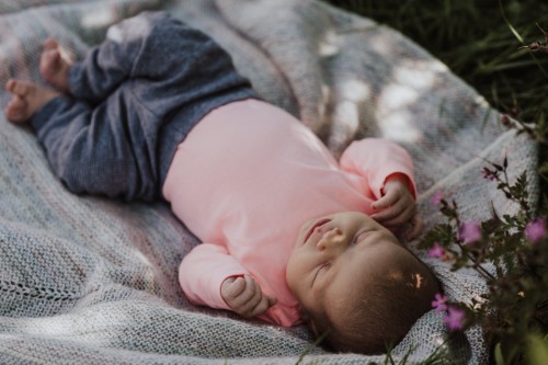 Ein kleines Baby liegt auf einer Decke zwischen den Blumen.