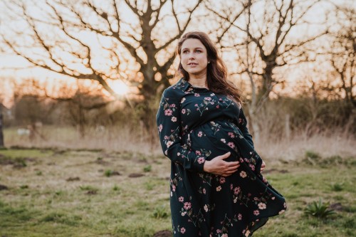 Eine schwangere Frau steht auf einem Feld und legt ihre Hände auf ihrem Bauch.