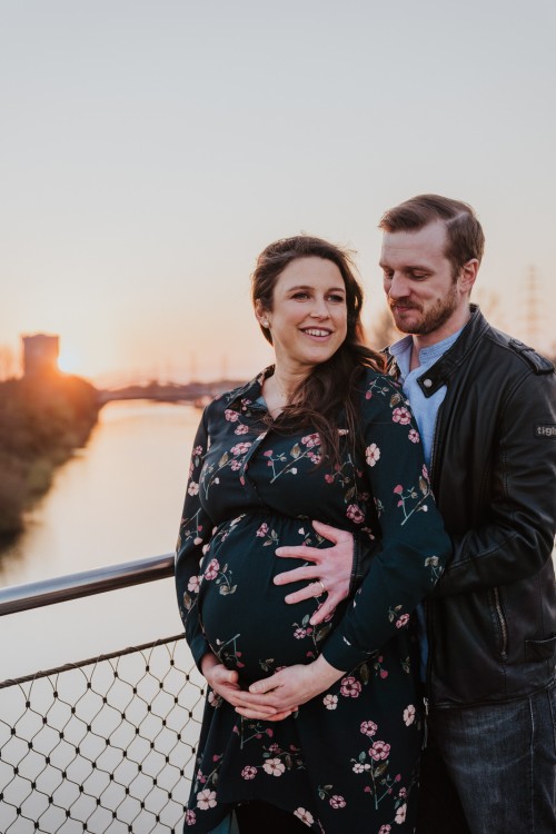 Ein Mann umarmt eine schwangere Frau und legt seine Hand auf ihrem Bauch.