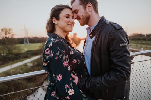 Eine schwangere Frau und ein Mann umarmen sich auf einer Brücke.