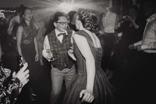 Ein schwarz-weißes Bild vom Brautpaar und deren Gästen tanzend auf der Tanzfläche.