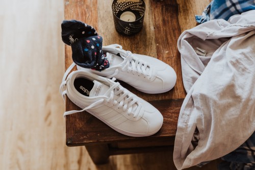 Weiße Sneaker mit bunten Socken auf einem Holztisch.