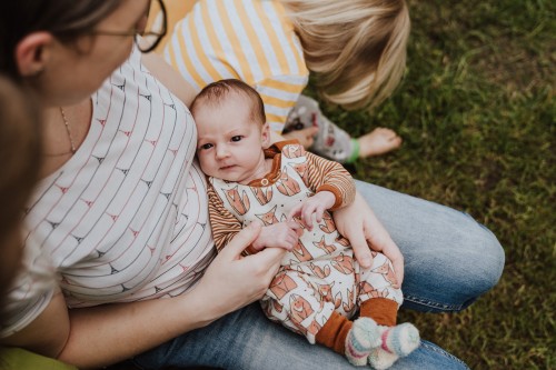 Eine Frau die ein Baby im Arm hält und ein spielendes Kind.