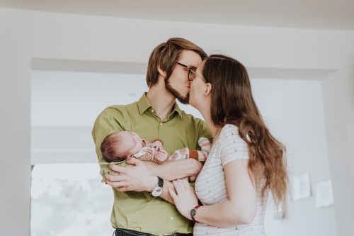 Eine Frau und ein Mann küssen sich, während er ein Baby auf dem Arm hält.
