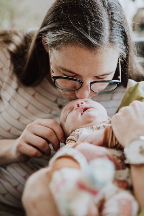 Eine Frau gibt einem neugeborenem Baby einen Kuss auf die Stirn.