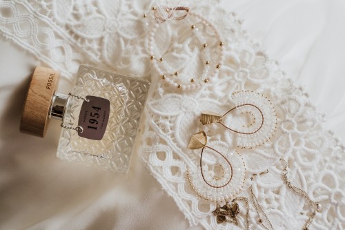 Schmuck und Parfum liegen auf einem Brautkleid.